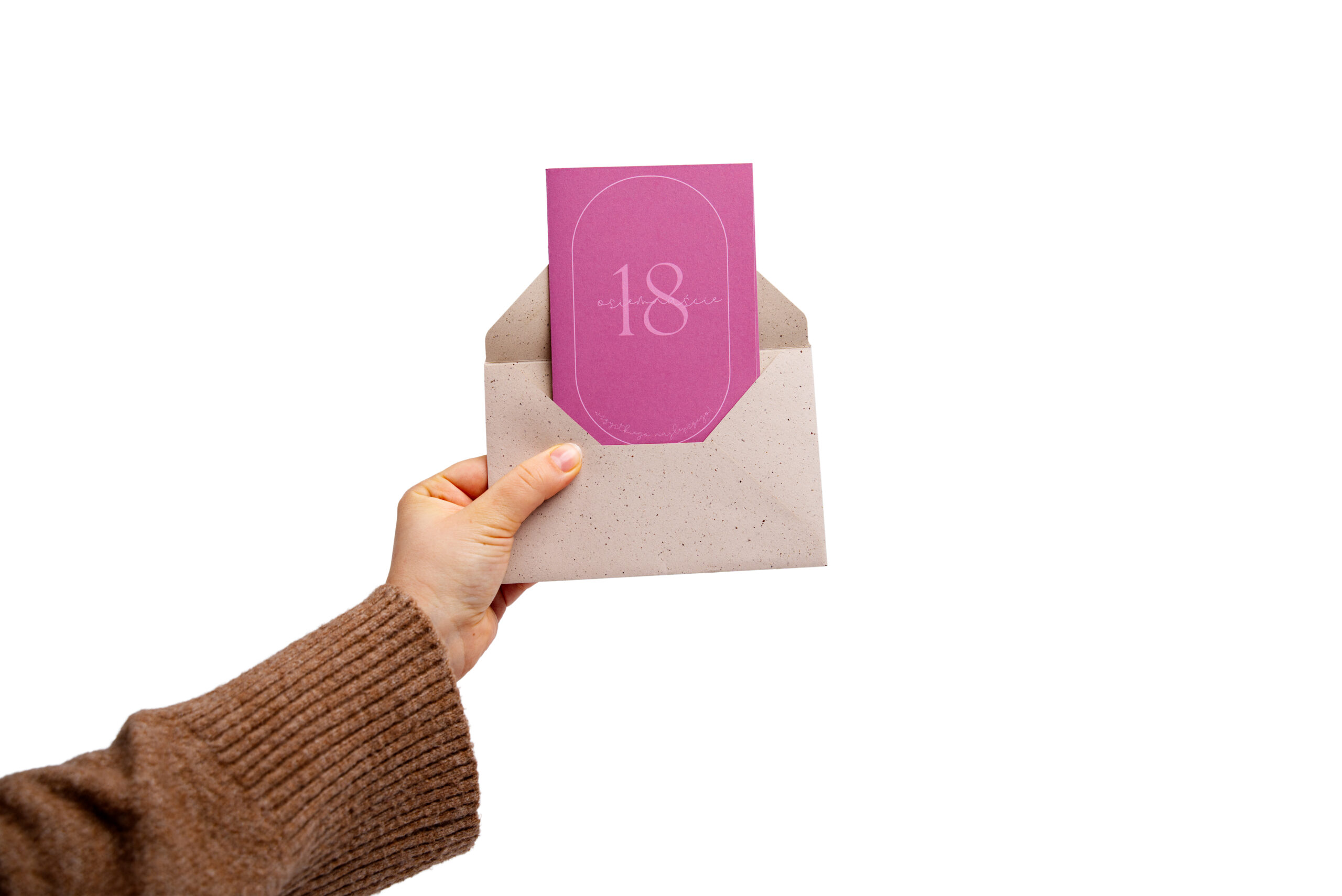 Różowo-fioletowa kartka na 18 urodziny z cyfrą 18 wychodząca z koperty kraft trzymanej w dłoni