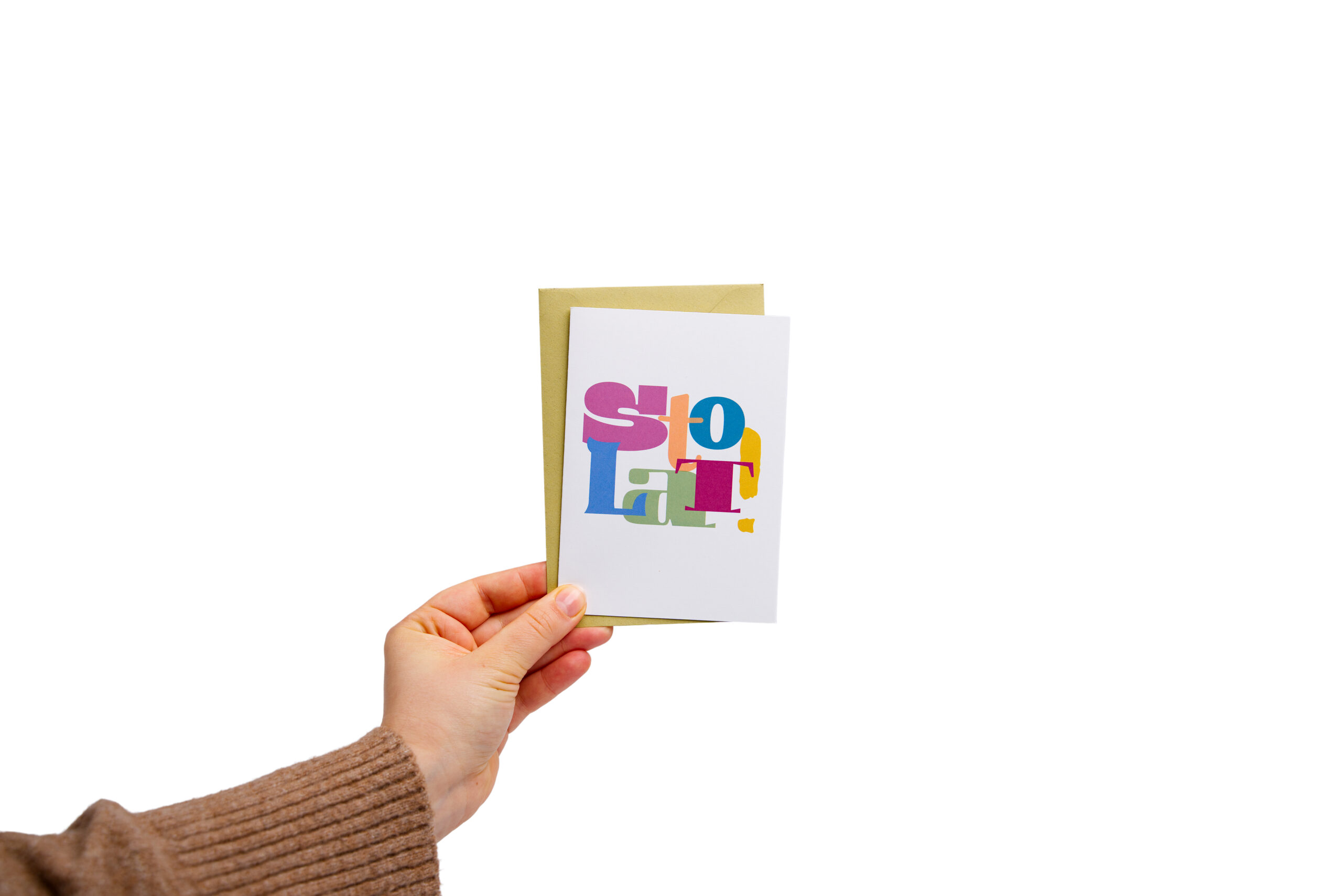 Biała kartka urodzinowa Sto Lat z kolorowym wielobarwnym napisem trzymana z oliwkową kopertą w dłoni